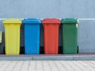 four assorted-color trash bins beside gray wall